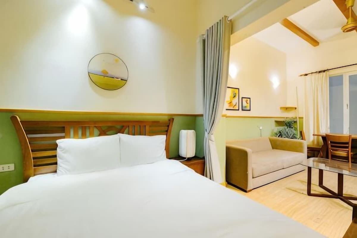 A hotel room with a bed, a sofa, a dining table, and a view of the outdoors.