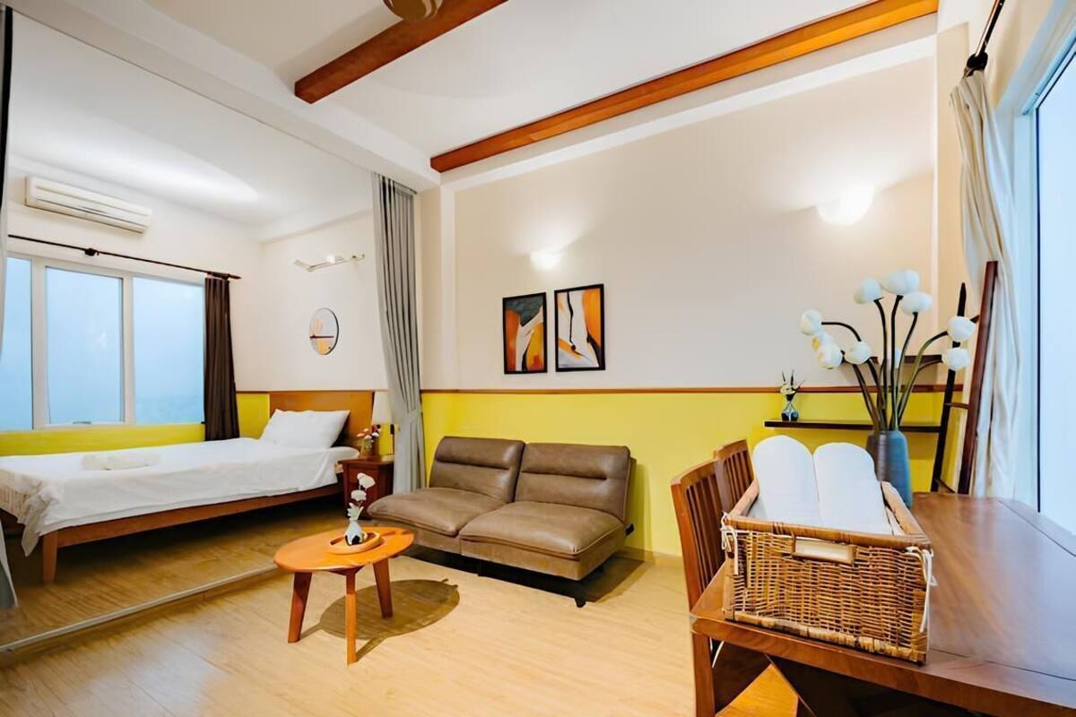 A room with a bed, a sofa, a dining table, and a small table with a vase.