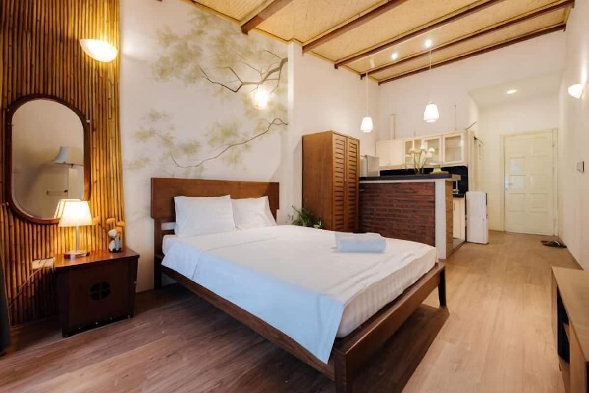 A bedroom with a wooden bed, a nightstand with a lamp, a wardrobe, and a mirror.