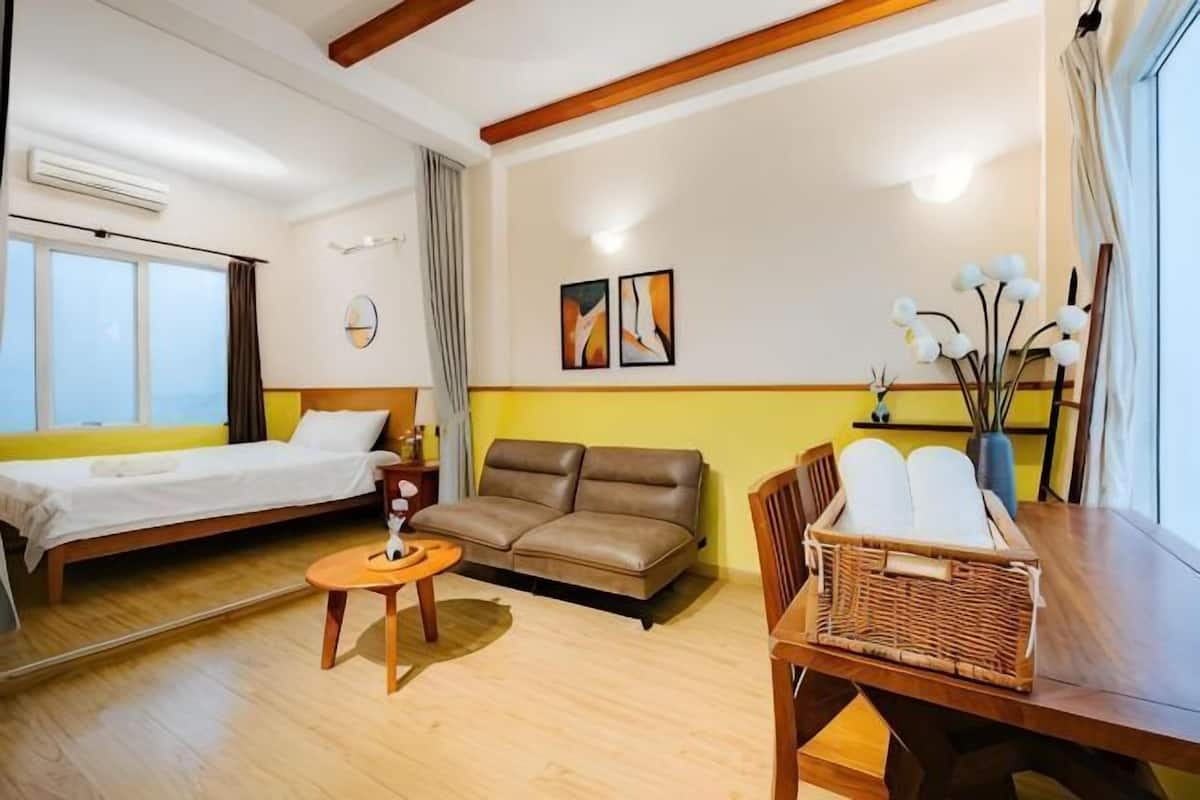 A room with a bed, sofa, dining table, and a window with curtains.