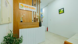 A reception desk with a wooden panel and a sign that reads "SUN GLOBAL". There is a potted plant to the left of the desk and a framed picture on the wall to the right. - Ha Noi Memory Apartel (Hanoi)