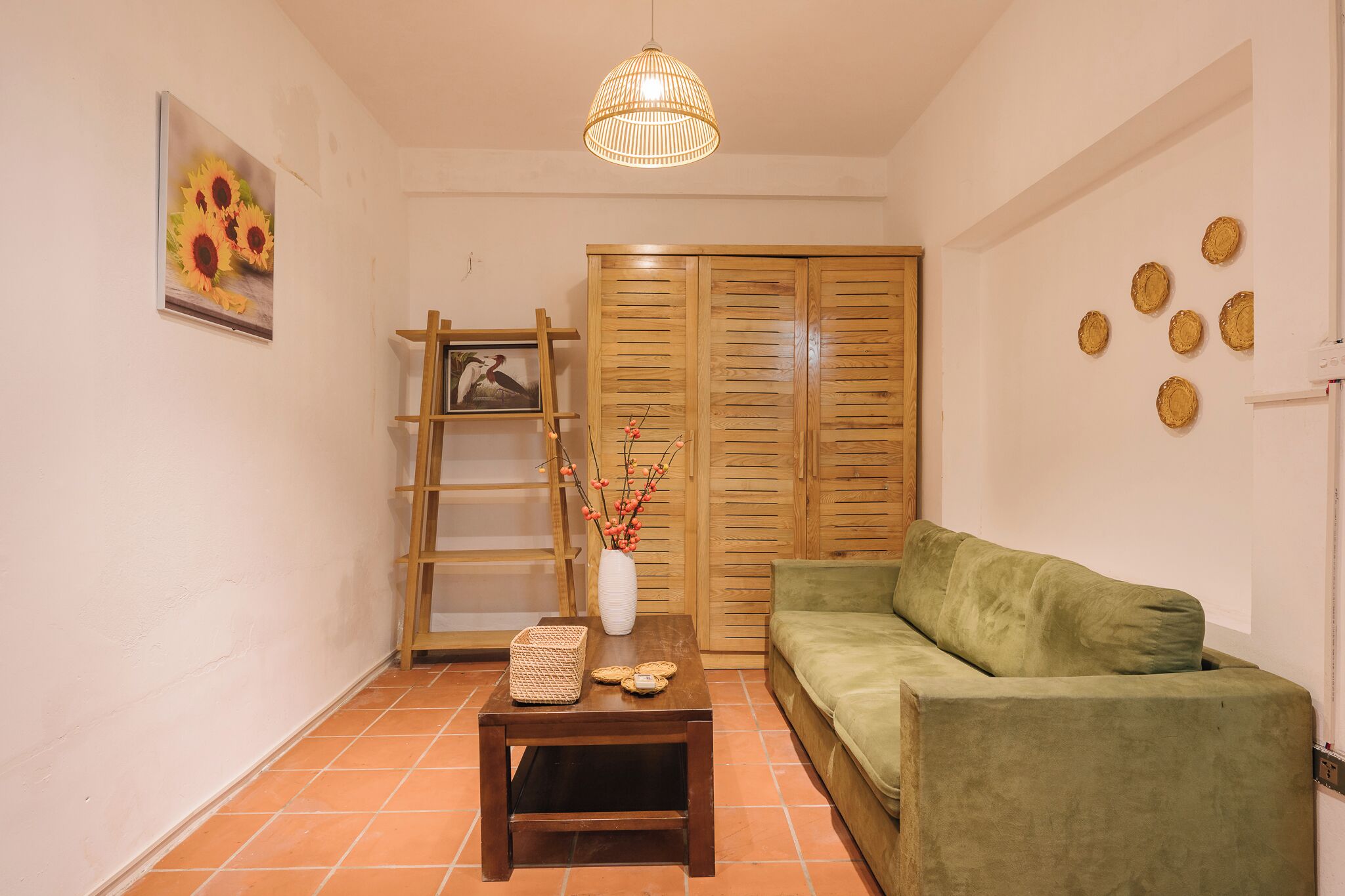 Ein Wohnzimmer mit einem grünen Sofa, einem Holztisch mit einer Vase und einem Korb, einem Holzschrank und einer Pendelleuchte.