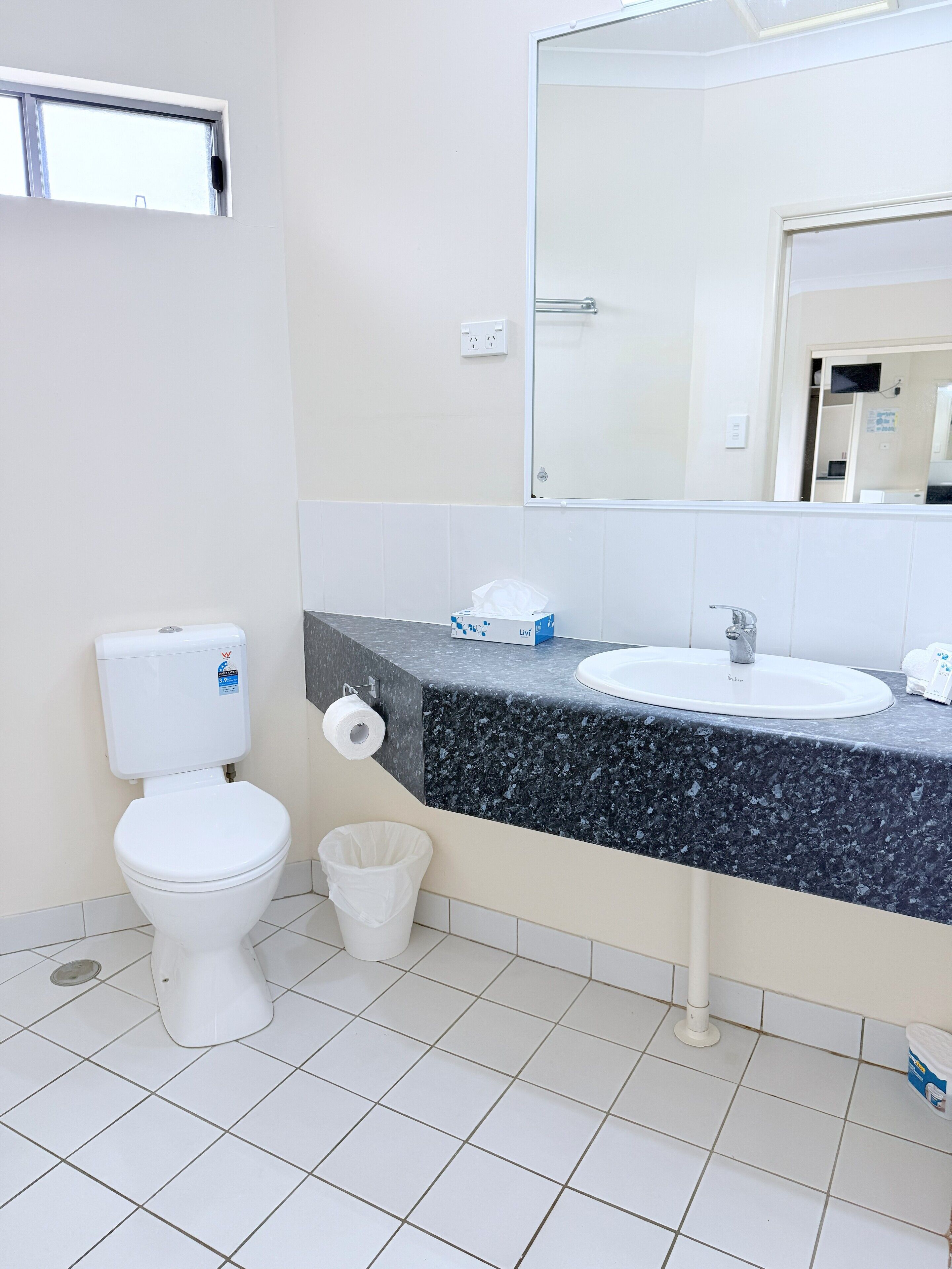 A bathroom with a toilet, sink, mirror, and a trash bin.