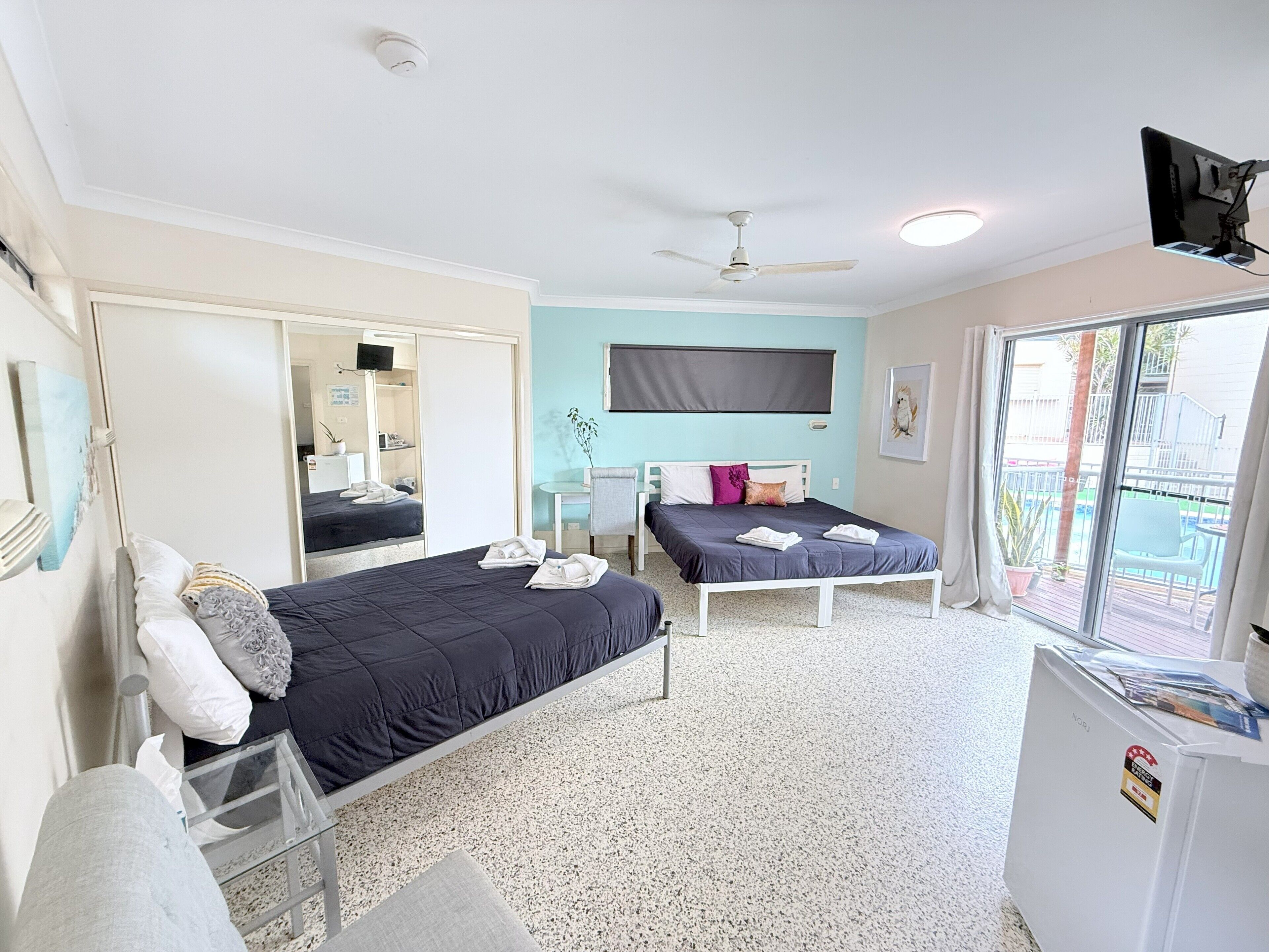 A bedroom with two beds, a desk, a chair, a TV, and a balcony with a view.