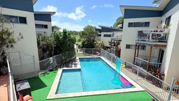 A swimming pool surrounded by a fenced area with green artificial turf, a small slide, and a few lounge chairs.