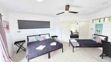 Un dormitorio con dos camas, un ventilador de techo, un televisor de pantalla plana y un espejo.