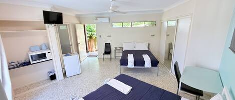 A hotel room with two beds, a small kitchenette, a TV, and a ceiling fan.