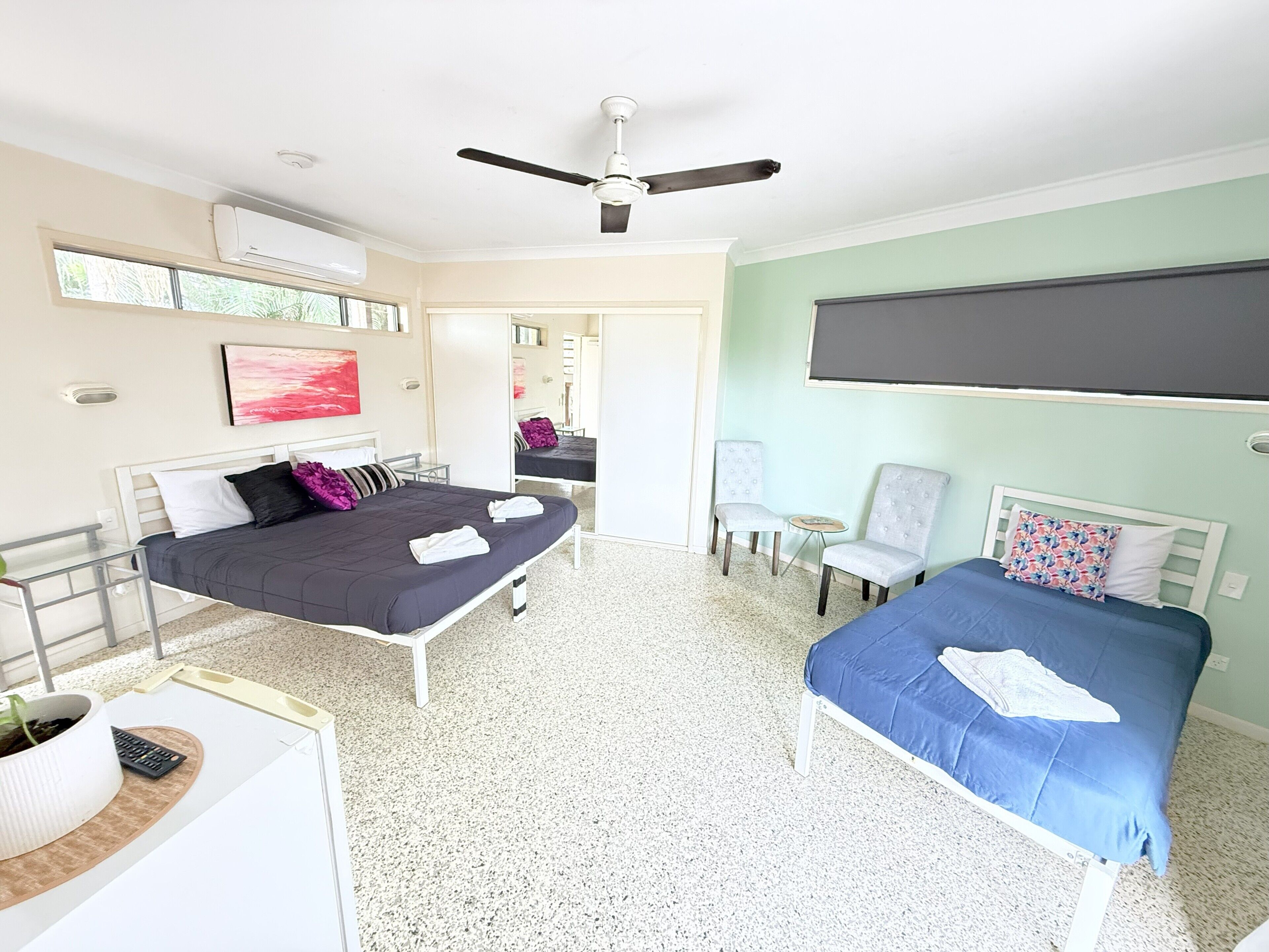 Una camera da letto con due letti, un ventilatore a soffitto, un condizionatore d'aria, un tavolino e una sedia.