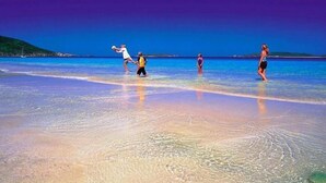 A beach scene with clear water and a person playing with a ball.