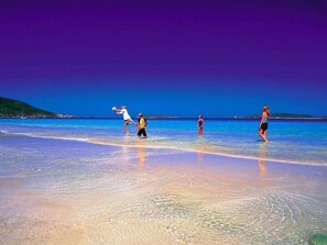 Une scène de plage avec une eau claire et une personne qui joue avec un ballon.