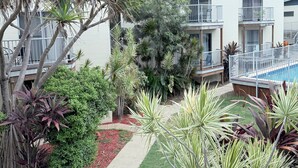 A modern building with multiple balconies, a swimming pool, and a variety of tropical plants. - Emu Park Beach Resort (Emu Park)