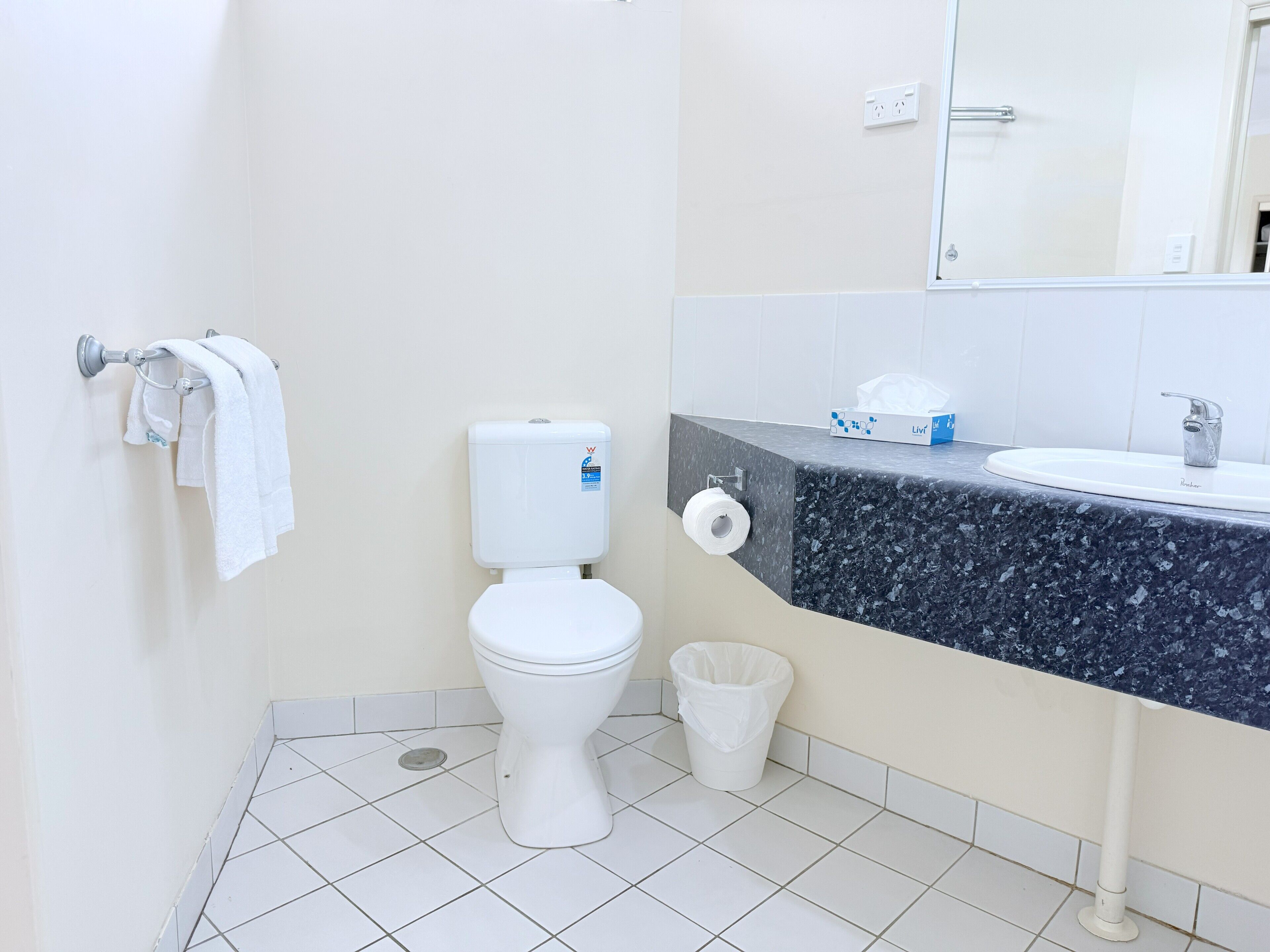 Une salle de bain équipée de toilettes, d’un lavabo, d’un miroir et d’une poubelle.
