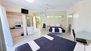 A hotel room with a bed, a desk, a chair, a TV, a ceiling fan, and a small kitchenette.