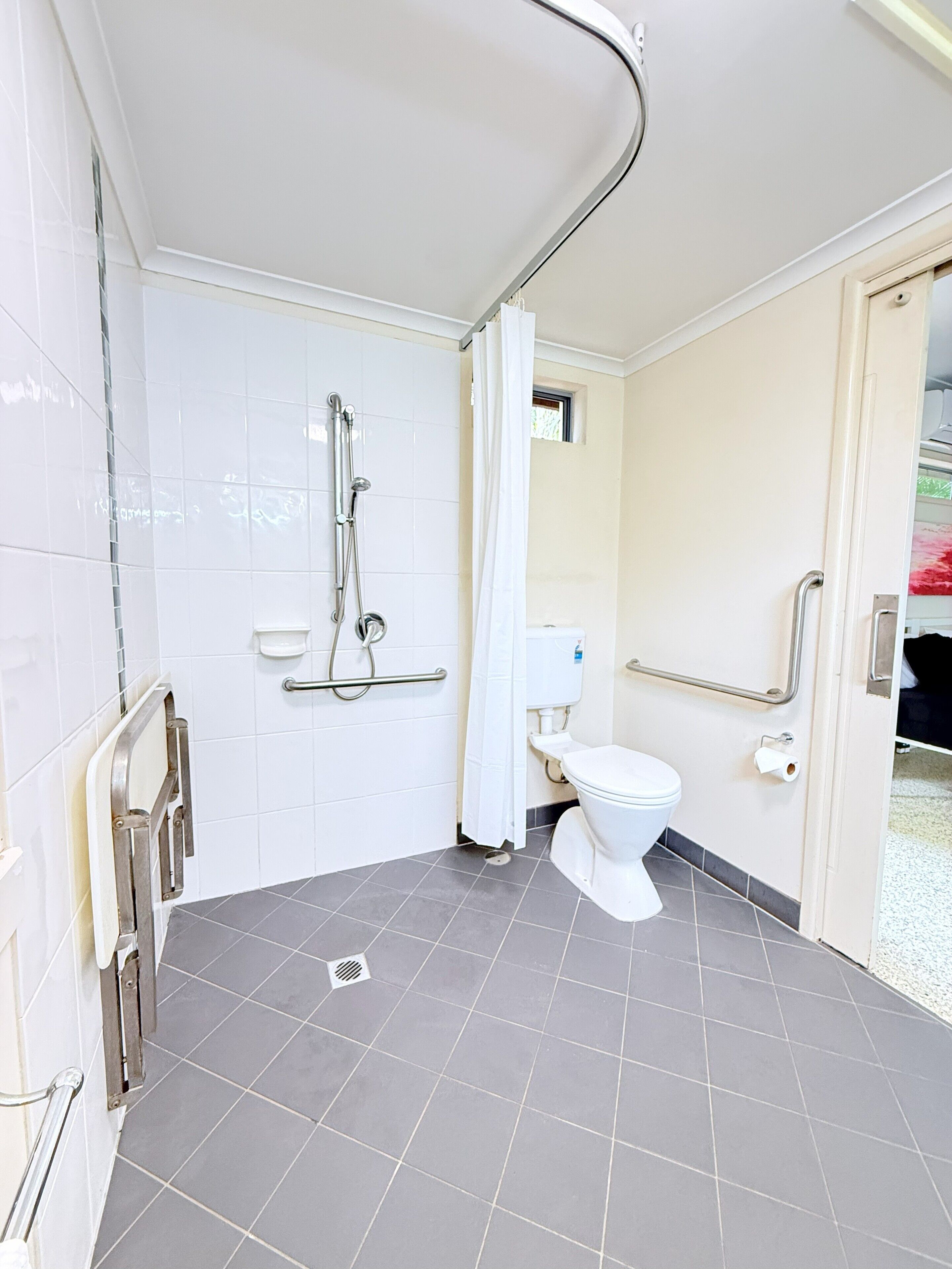 Un baño con ducha, inodoro y barras de apoyo.