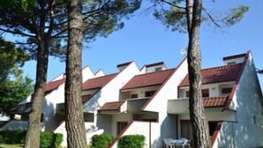 A row of white buildings with red roofs and balconies, surrounded by trees and grass.