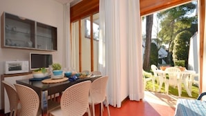 A dining area with a table set for four, surrounded by wicker chairs. A microwave and a glass cabinet are visible on the wall.