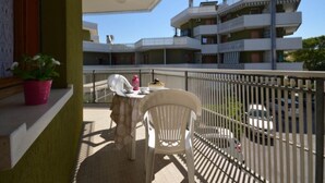 Un balcon avec une table et des chaises, un pot de fleurs et une vue sur un immeuble à plusieurs étages.