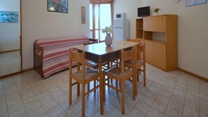 Une petite pièce bien rangée, avec une table à manger en bois, quatre chaises, un canapé à rayures, un téléviseur posé sur un meuble en bois et une horloge au mur.