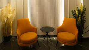 A modern lobby with two orange chairs, a small round table, and a decorative wall panel. - Hotel Millennium  (Hisar)