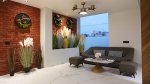 A modern living room with a brick wall, two round wall decorations, a grey sofa, a coffee table, and a ceiling fan. - Hotel Millennium  (Hisar)