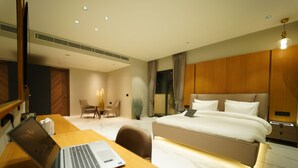 A modern hotel room with a large bed, a desk with a laptop, a chair, and a small table with a lamp. - Hotel Millennium  (Hisar)