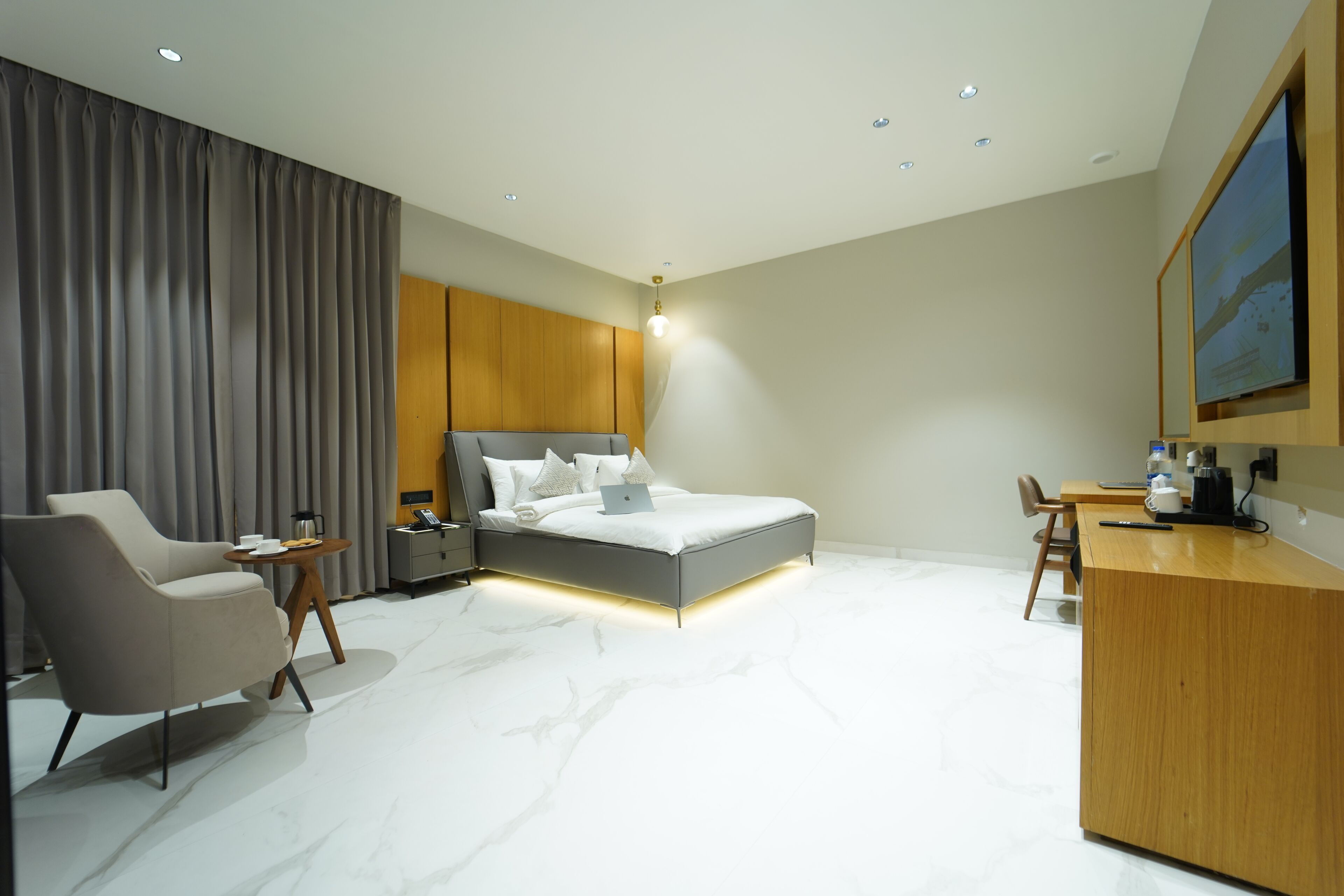 A modern hotel room with a bed, a desk, a chair, and a large window.