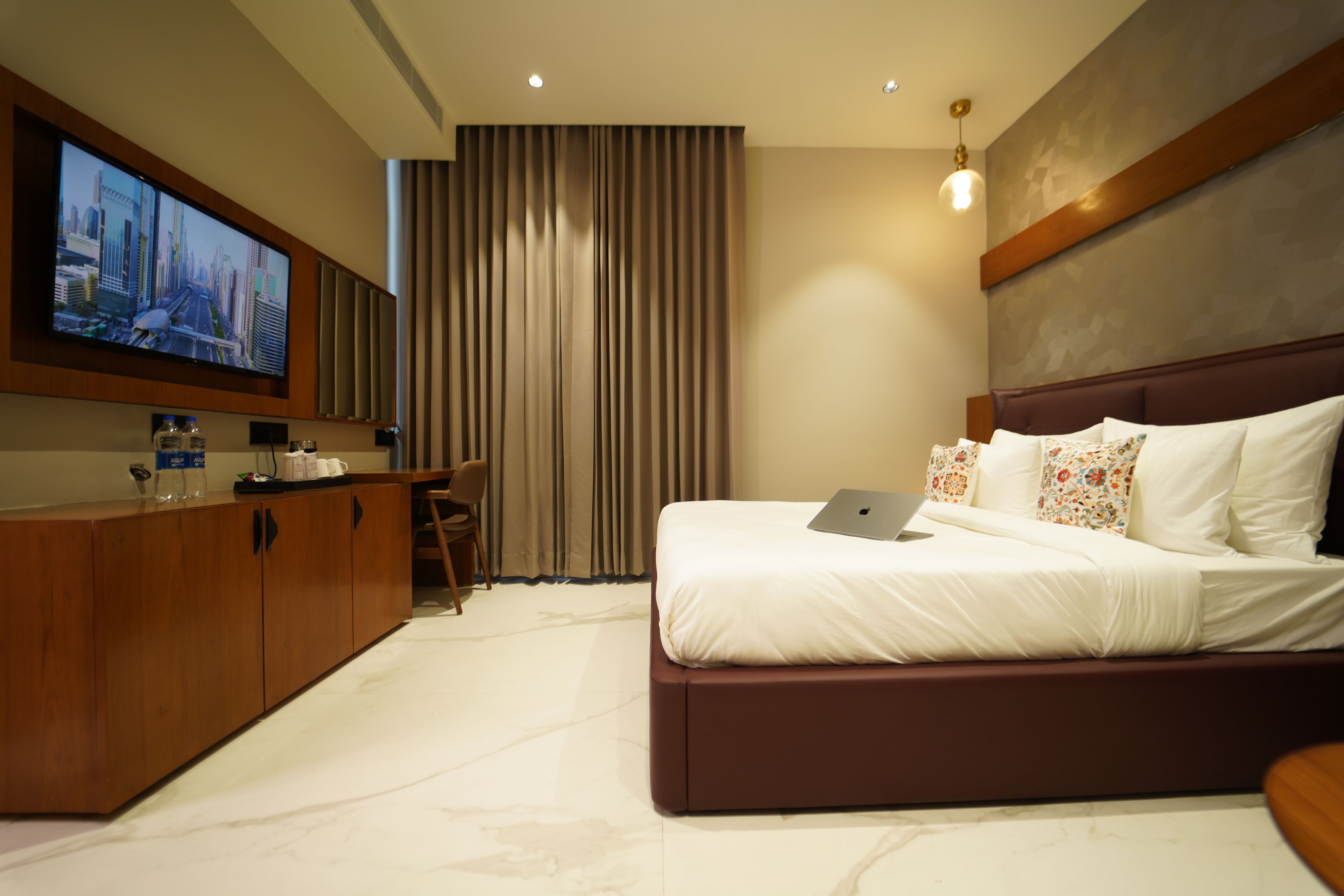 Een moderne hotelkamer met een groot bed, een bureau met een laptop, een flatscreen-tv en een minibar.