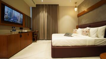 Een moderne hotelkamer met een groot bed, een bureau met een laptop, een flatscreen-tv en een minibar.