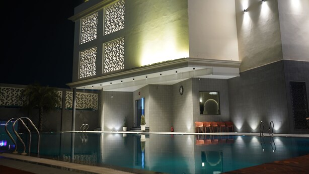 A modern hotel with a pool area, including a glass-enclosed pool, seating by the pool, and a well-lit entrance. - Hotel Millennium  (Hisar)