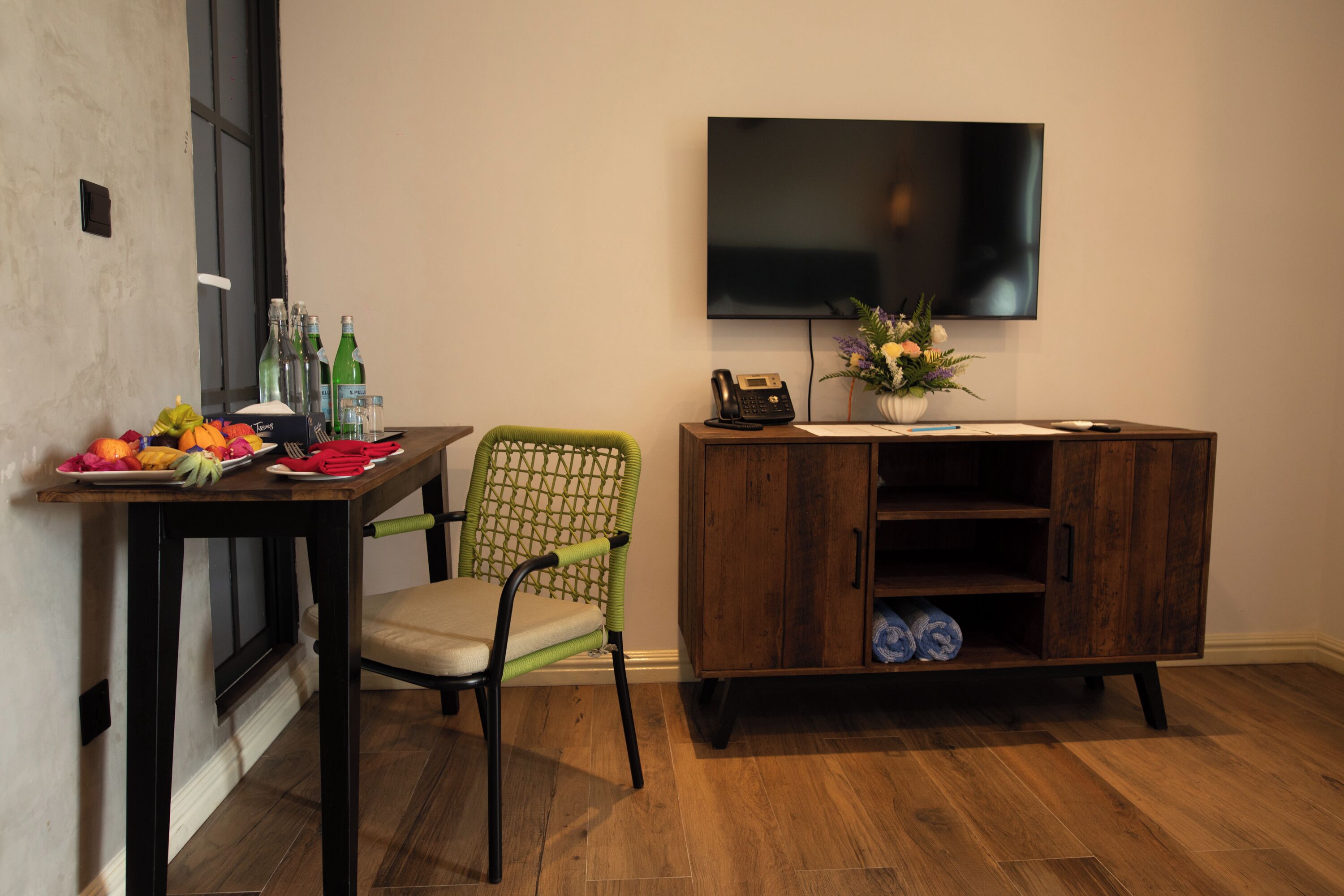 Una habitación con una mesa de comedor, una silla verde, un armario de madera, un televisor de pantalla plana y un jarrón con flores.