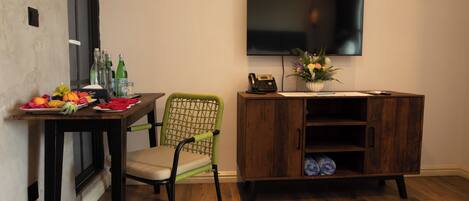 A room with a dining table, a green chair, a wooden cabinet, a flat-screen TV, and a vase with flowers.