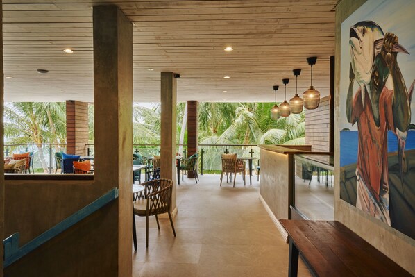 A restaurant with wooden ceiling beams, a mural of a bird, and outdoor seating with palm trees. - Beach Hotel Dhigurah (Dhigurah)