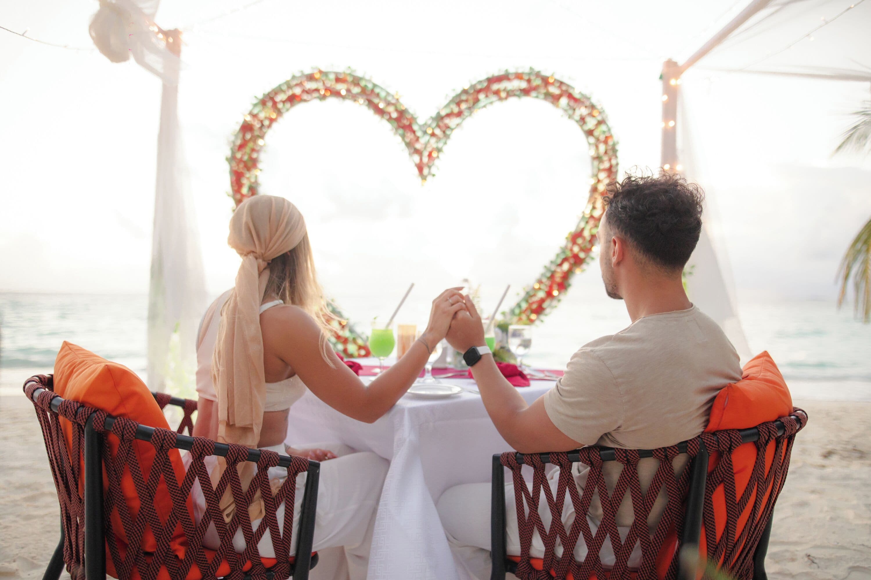 A couple dining at a table with a heart-shaped decoration in the background.