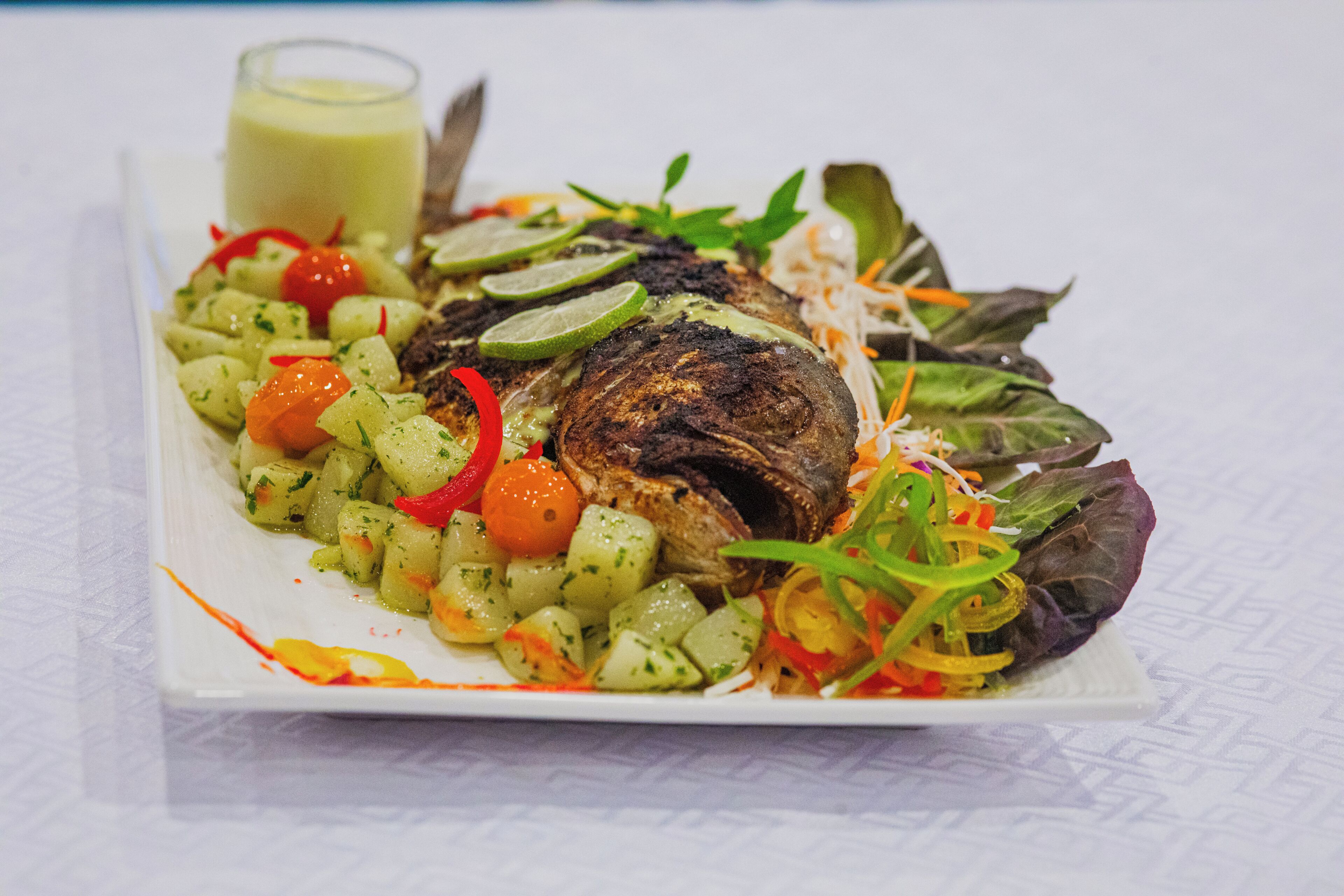 Un plato con pescado a la parrilla, patatas en cubos y una variedad de verduras.