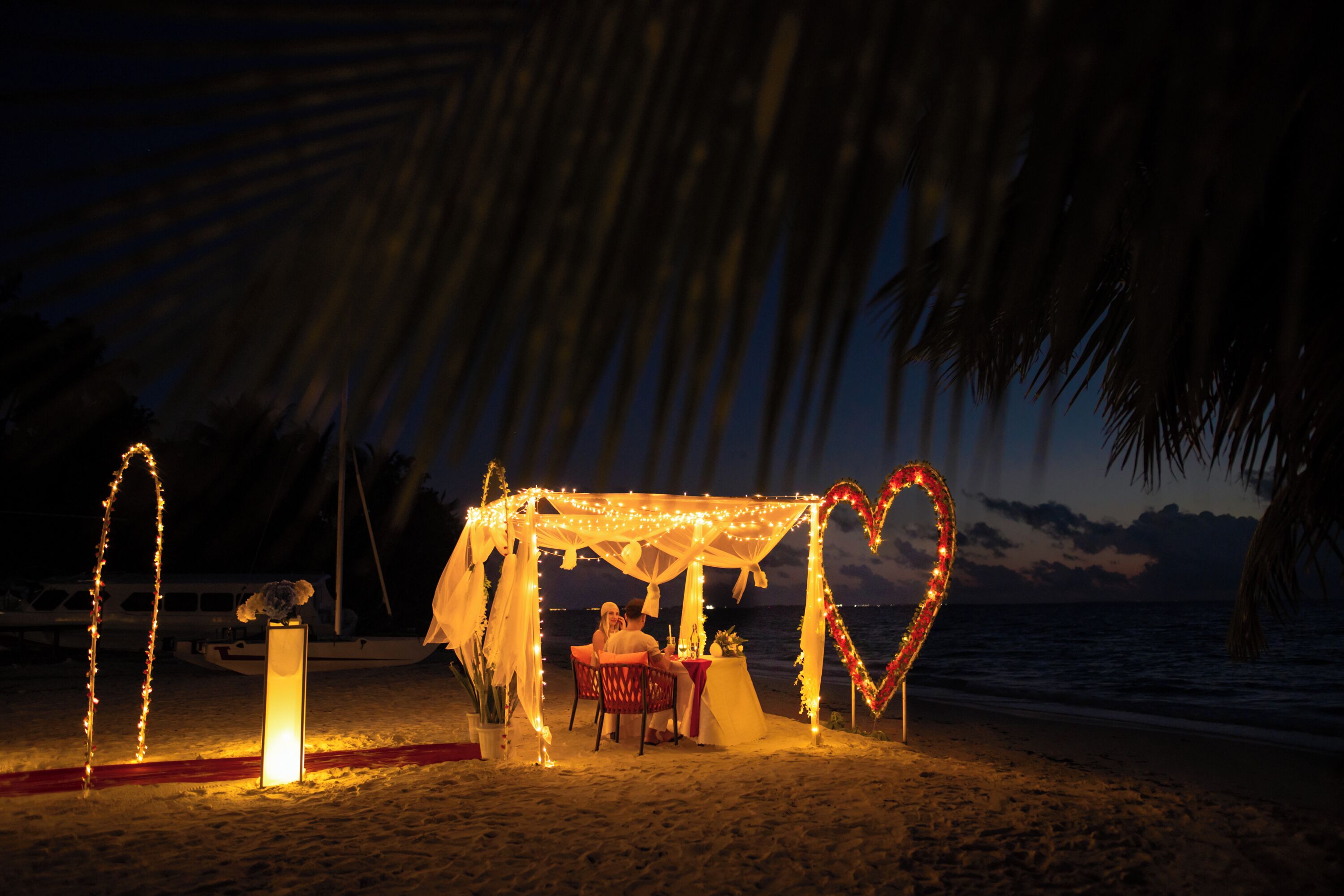 A beachside gazebo with a heart-shaped decoration, a dining table, and chairs.