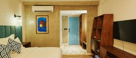 A hotel room with a bed, a ceiling fan, a TV, a wooden bookshelf, and a painting on the wall.