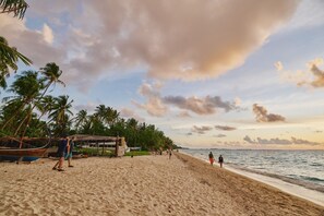 Une plage bordée de palmiers, une structure à toit de chaume et des bateaux.