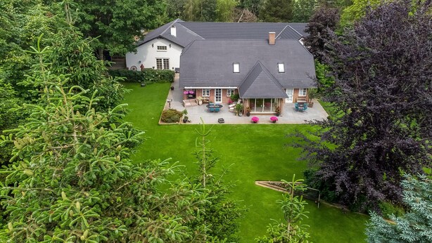 A large house with a spacious patio, surrounded by lush greenery.