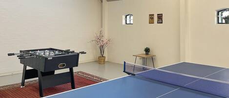 A room with a foosball table, ping pong table, and a small table with a plant.