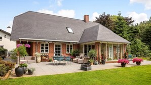 A two-story house with a brick exterior, a covered patio with outdoor furniture, and a well-maintained lawn.