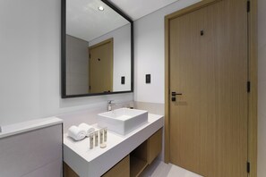 Ein modernes Badezimmer mit einem weißen Waschbecken, einem großen Spiegel und einer Holztür.