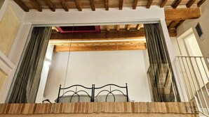 Ein Zimmer mit einem Bett, Holzbalkendecke und Blick durch ein Fenster mit Vorhängen.