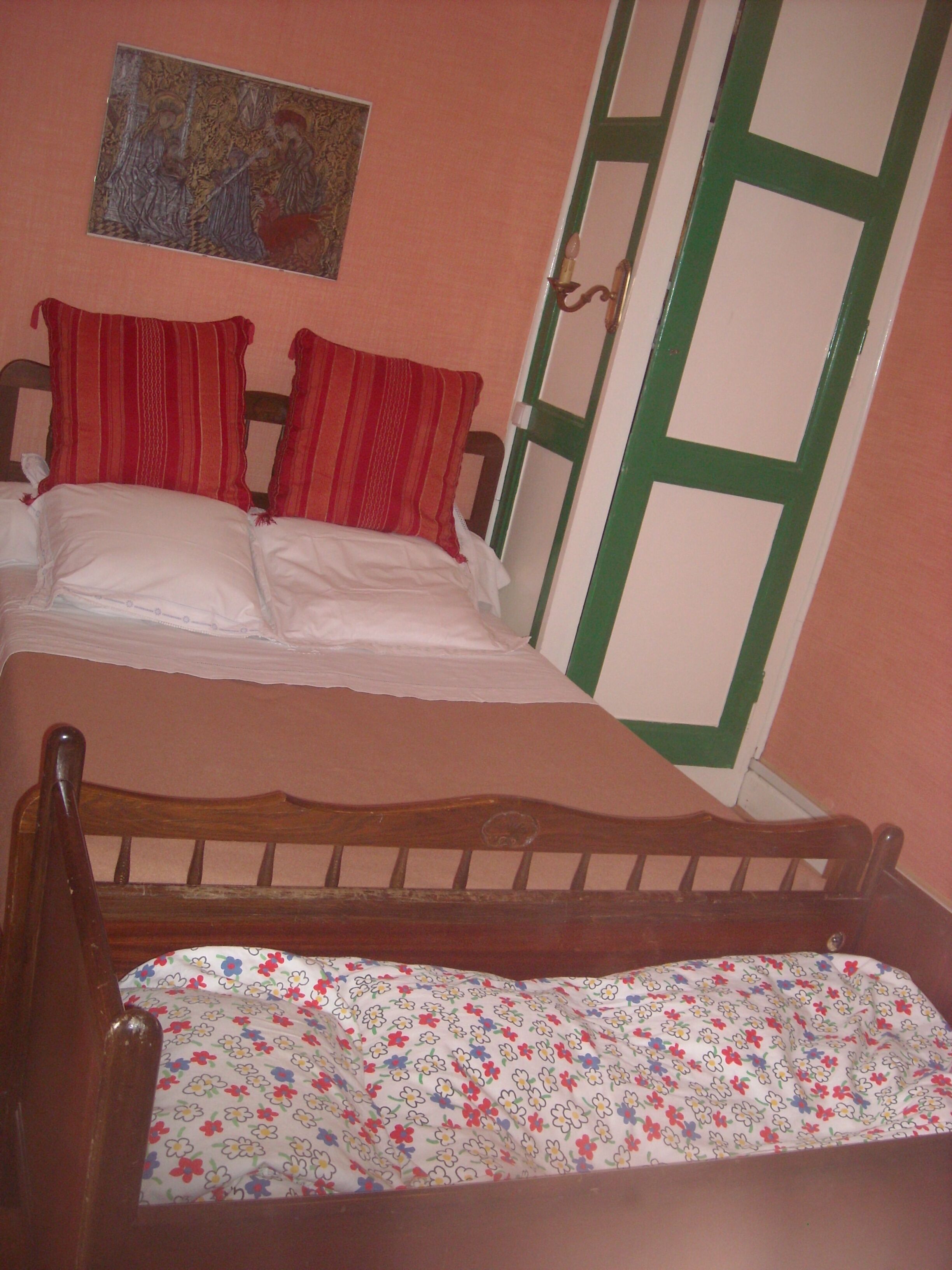 Ein Schlafzimmer mit einem hölzernen Bett, zwei roten Kissen, einer blumigen Tagesdecke und einem Bild an der Wand.