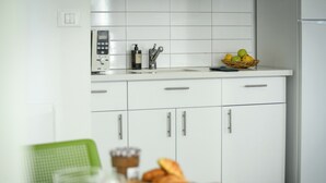 A modern kitchen with white cabinets, a sink, and a basket of fruits on the countertop. - 1 BR Apt w living room & learning area (Tel Aviv)