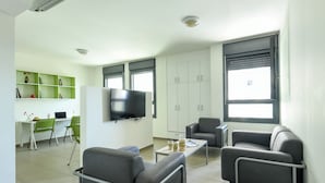 A modern living room with a flat-screen TV, grey sofas, a coffee table, and a green shelving unit. - 1 BR Apt w living room & learning area (Tel Aviv)