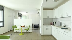 A modern kitchen with white cabinets, a dining area with green chairs, and a small table. - 1 BR Apt w living room & learning area (Tel Aviv)