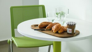 A round white table with a wooden board holding croissants and a jar of jam. A green chair is behind the table. - 1 BR Apt w living room & learning area (Tel Aviv)