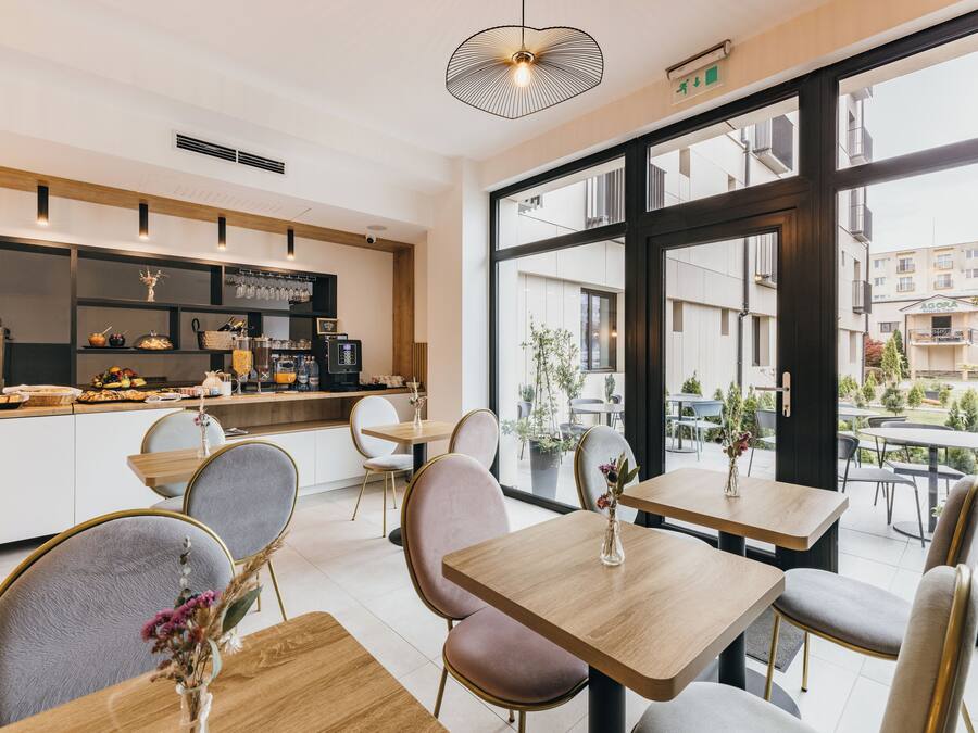 A modern cafe with wooden tables and chairs, a counter with a coffee machine, and large windows offering a view of the city.