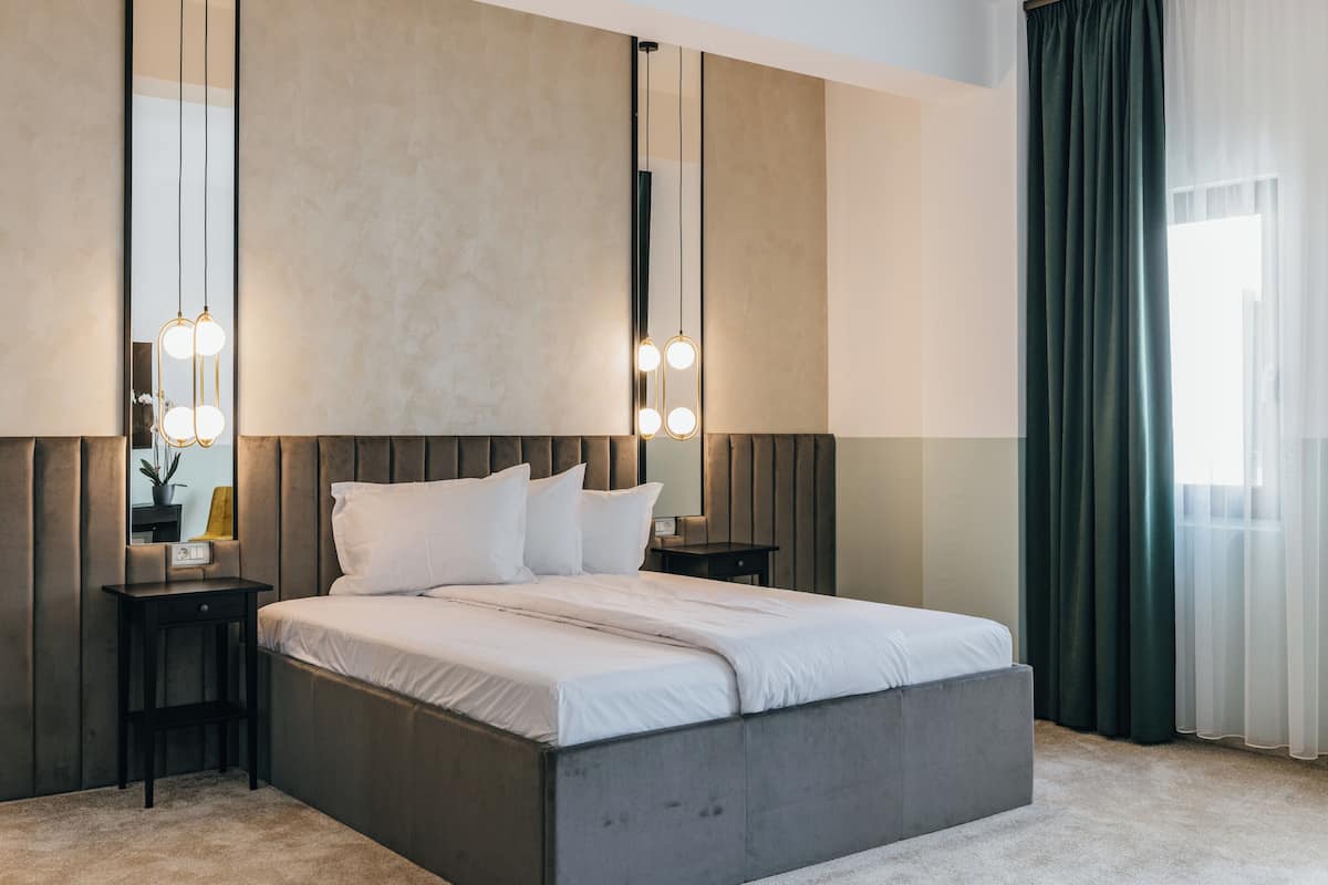A modern bedroom with a large bed, bedside tables, a mirror, and pendant lights.