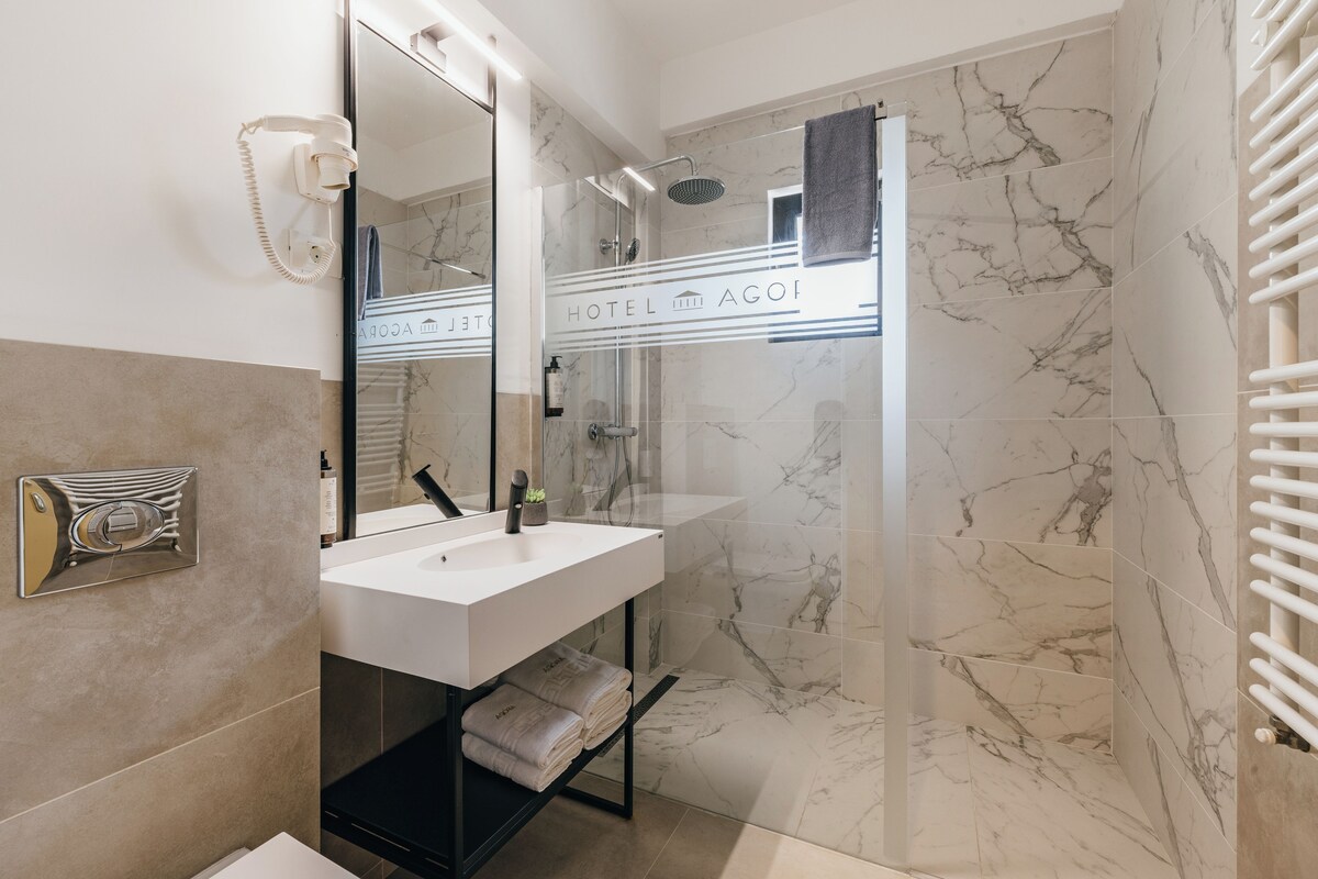 Un baño moderno con un lavamanos blanco, una ducha con cerramiento de vidrio y paredes de mármol.